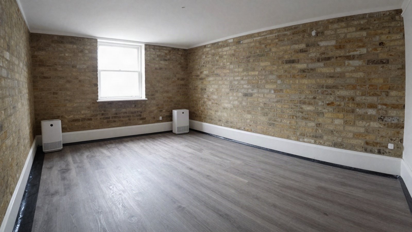 A converted Victorian cellar with painted brick walls and a newly laid grey oak-effect rigid vinyl plank floor over a black damp-proof membrane