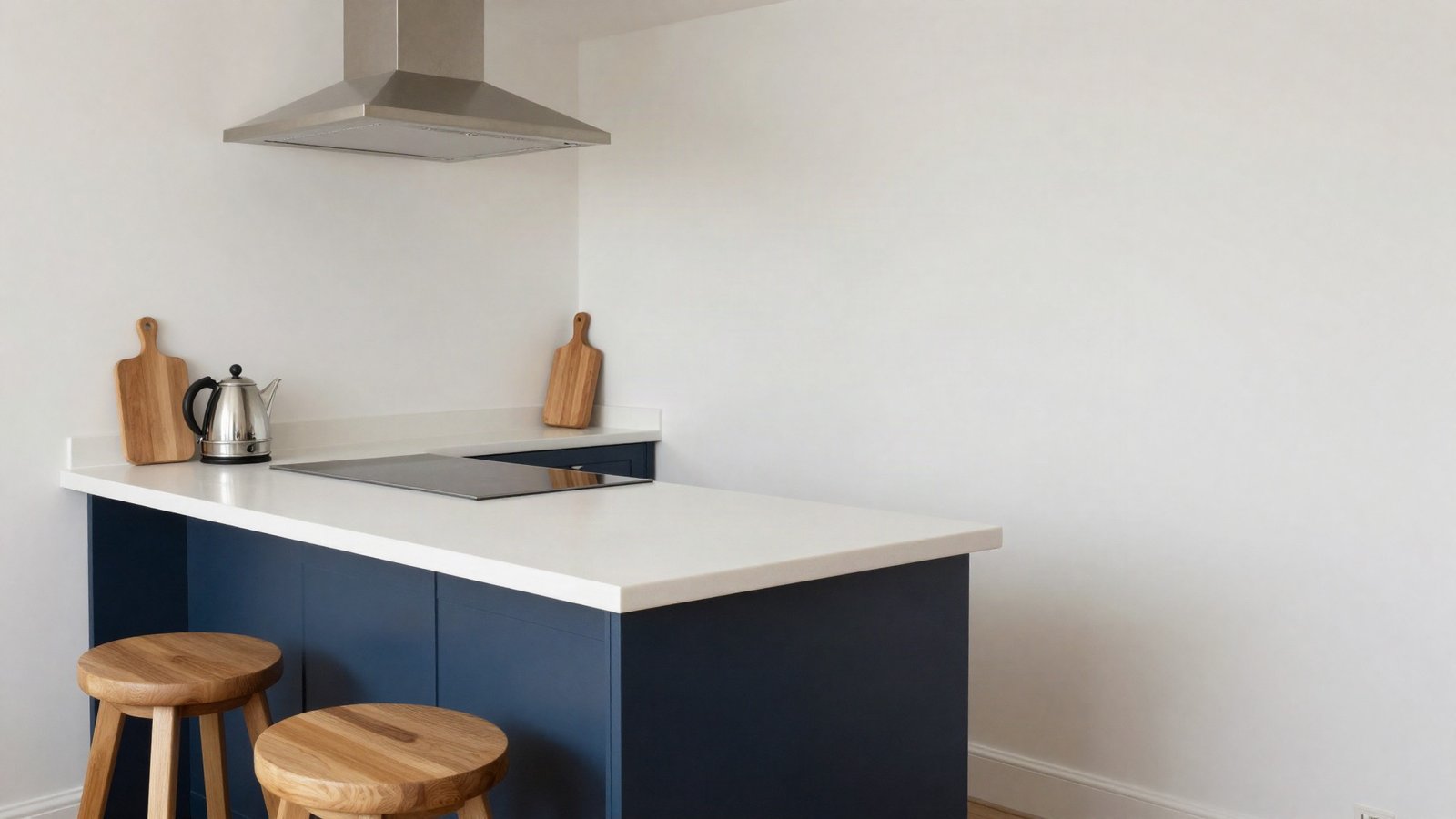 A navy shaker kitchen island with a white quartz worktop and two oak bar stools, beside a run of wall units in a bright UK kitchen