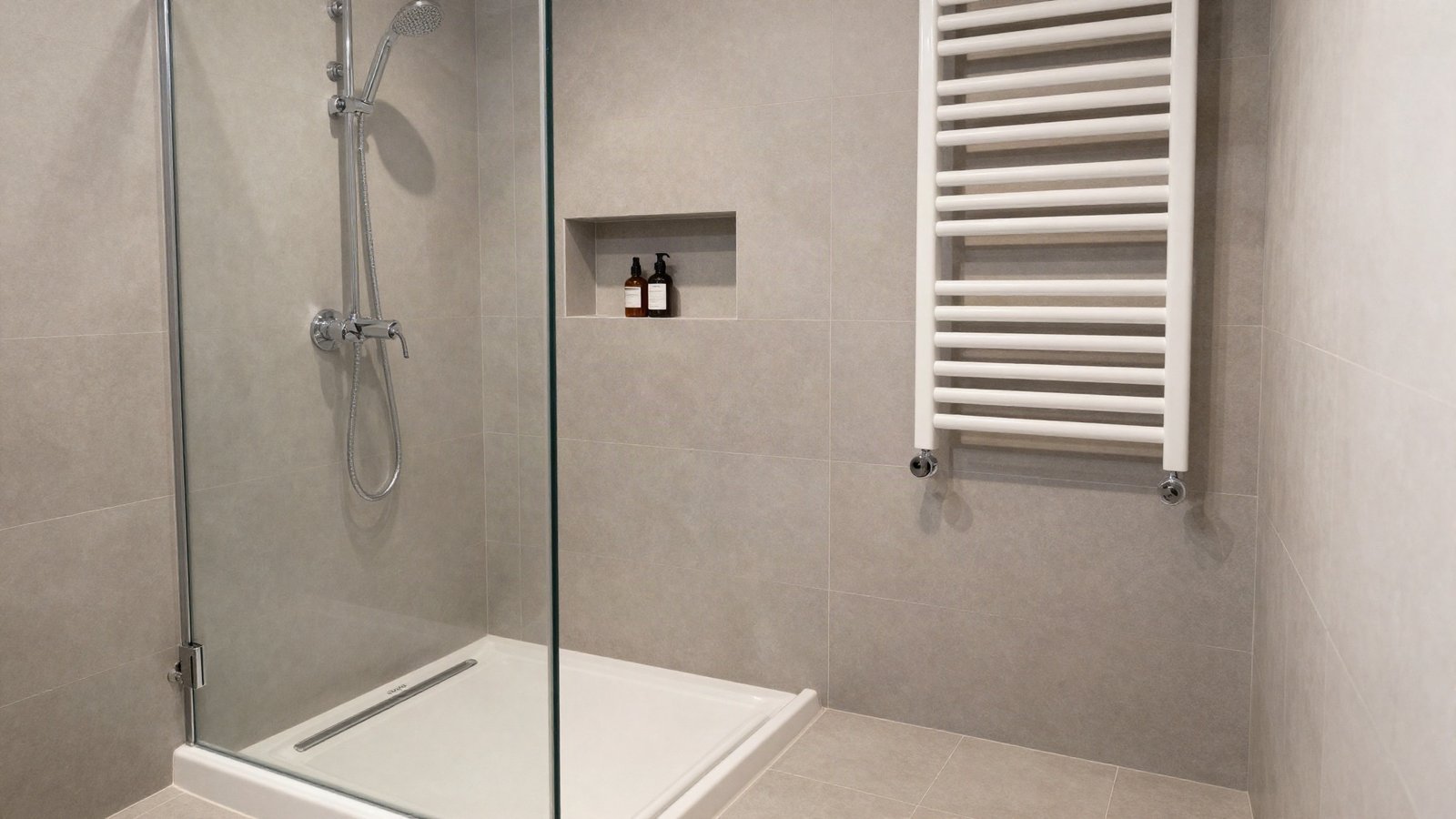 A walk-in shower with a frameless glass panel, large-format porcelain wall tiles and a linear drain in a small UK bathroom