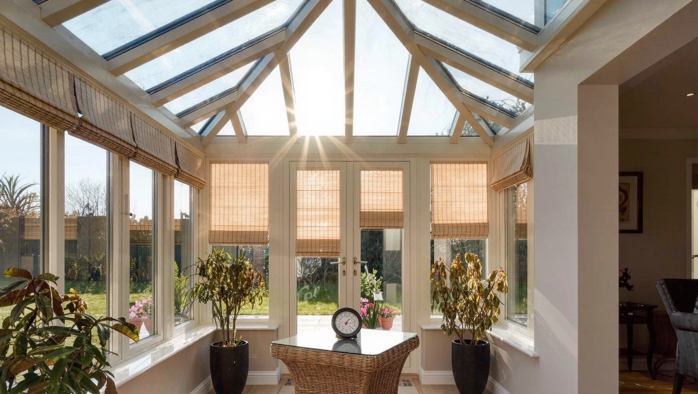 Bright UK conservatory with a glazed roof, cream pleated blinds and wicker furniture in strong summer sunlight